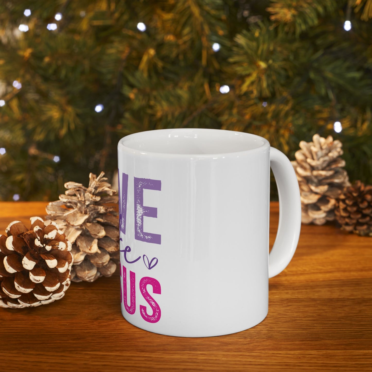 White mug with "love us" text and hearts, with pinecones and Christmas lights.