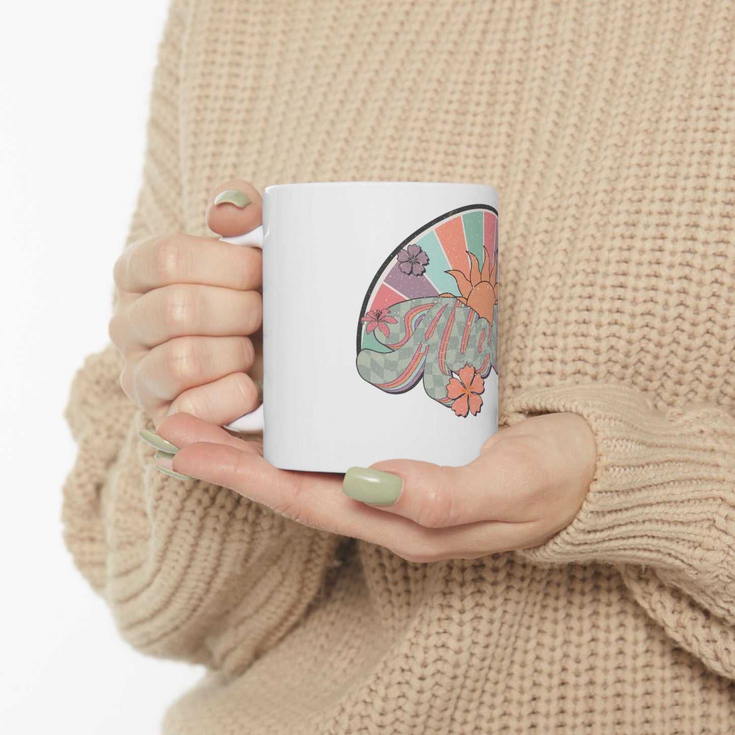 White mug with a colorful sun and floral design held by hands.