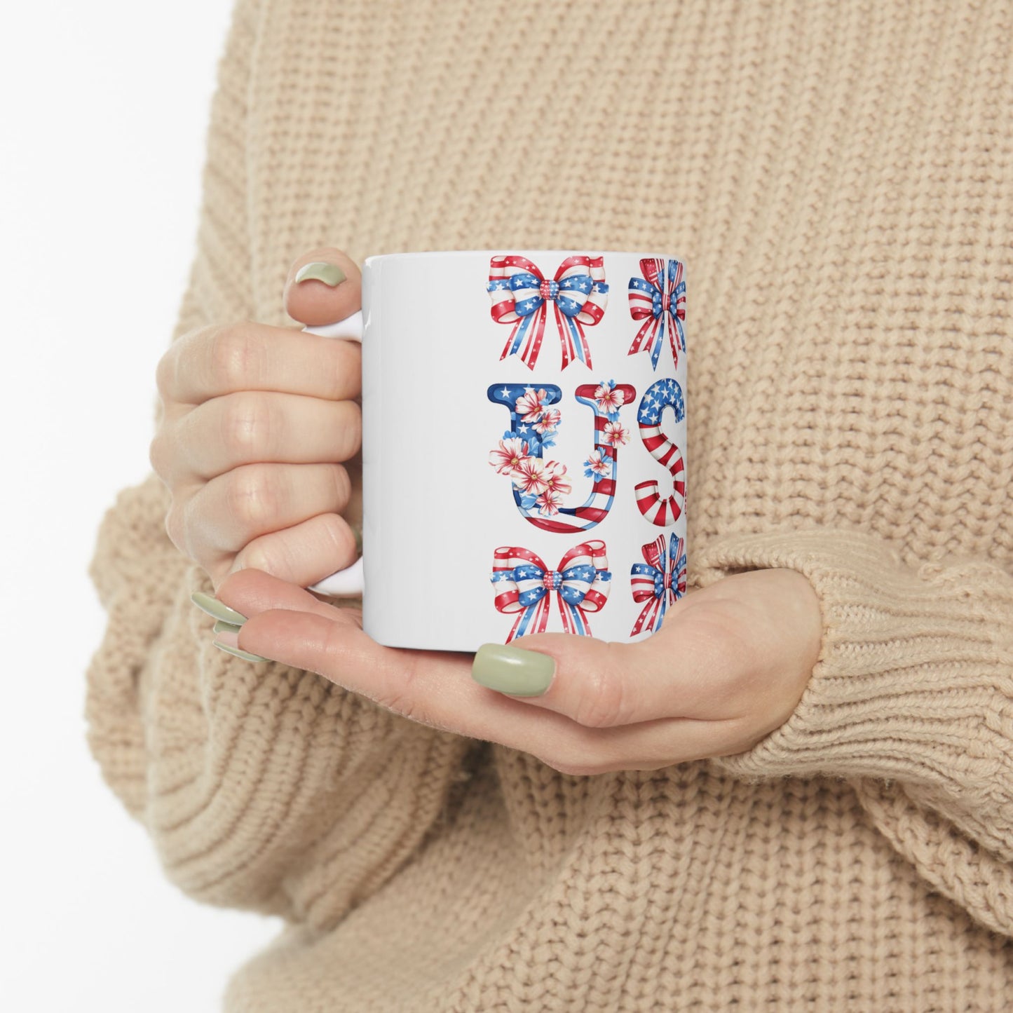 White mug with "US" and patriotic bows, held by hands.