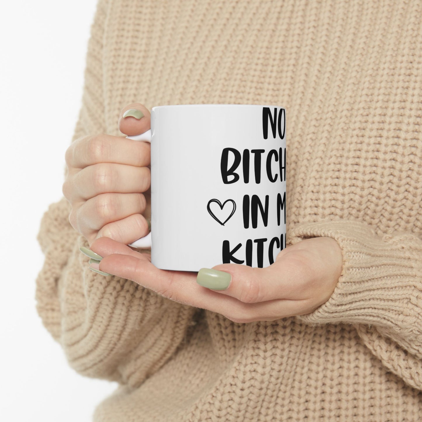 White mug with black text "NO BITCH IN MY KITCHEN" held by hands.