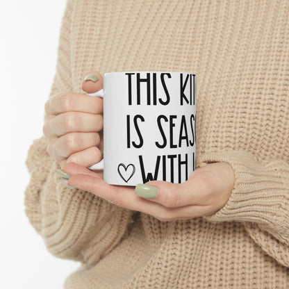 White mug with black text "THIS KITCHEN IS SEASONED WITH LOVE" and a heart.