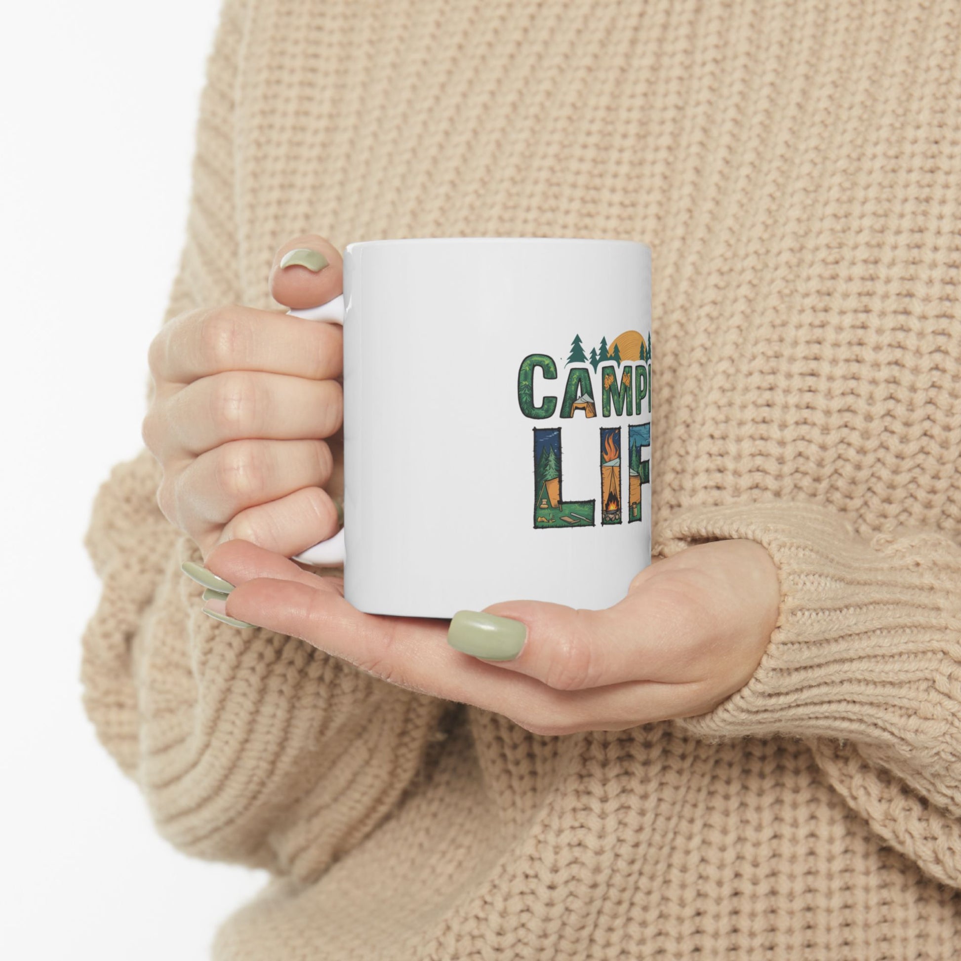 White mug with "CAMPING LIFE" text and forest graphics held by a person.