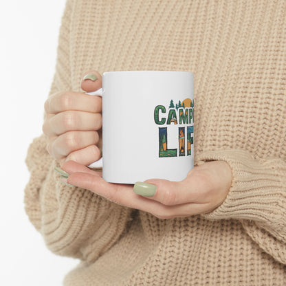 White mug with "CAMPING LIFE" text and forest graphics held by a person.
