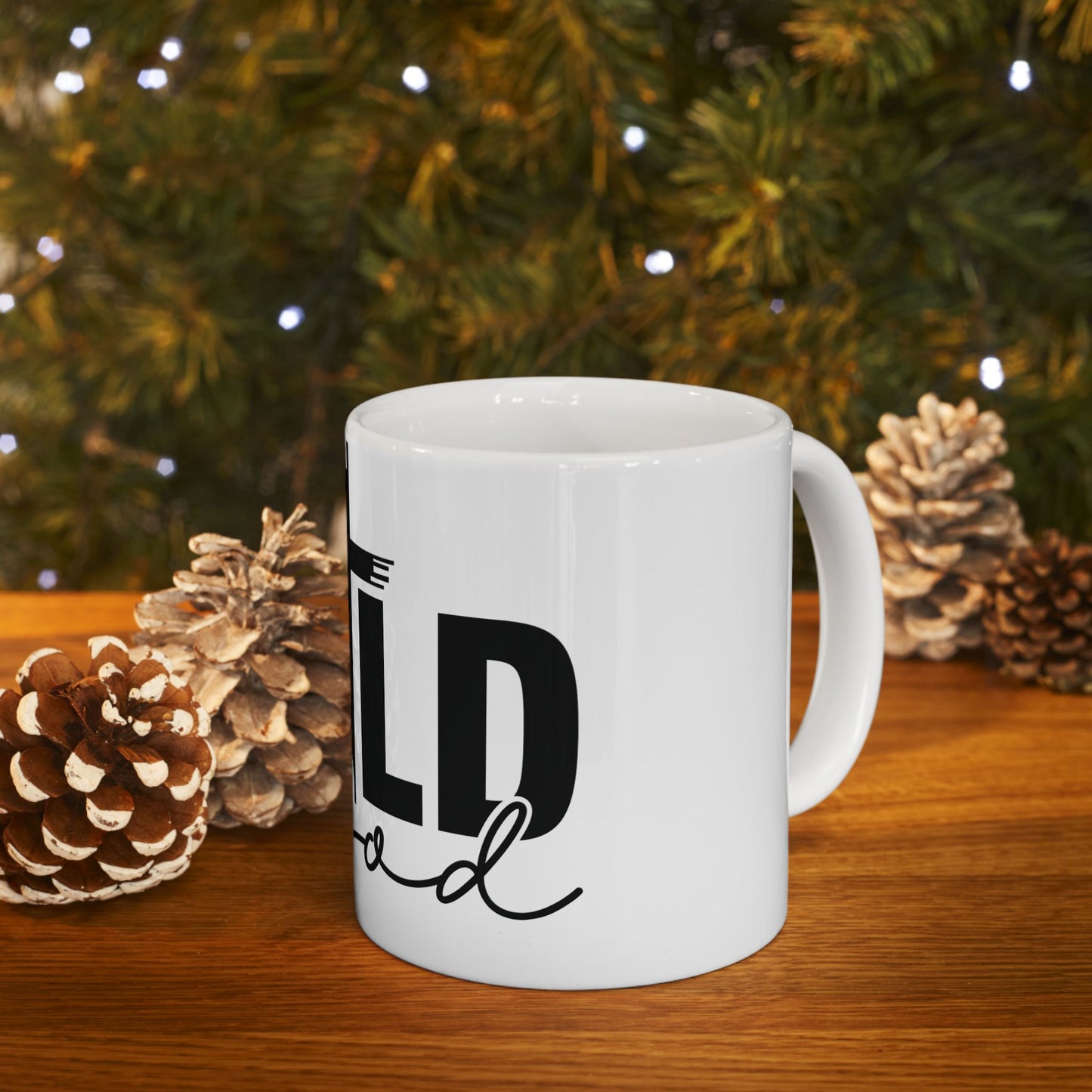 White mug with "WILD" text, pinecones, and blurred Christmas tree background.