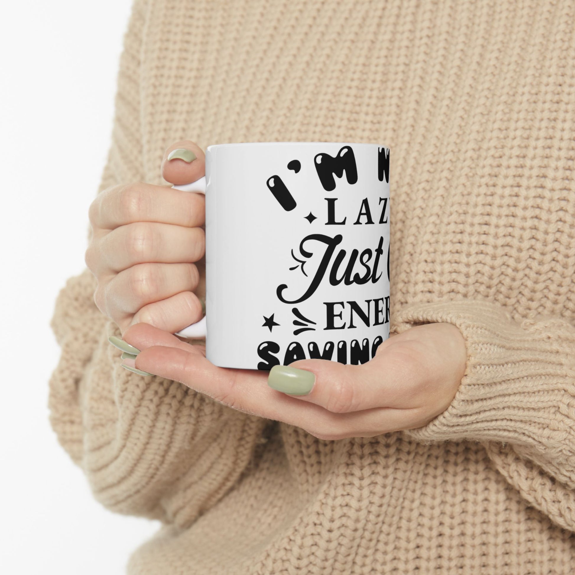 White mug with "I'm Not Lazy Just Saving Energy" text held by hands.