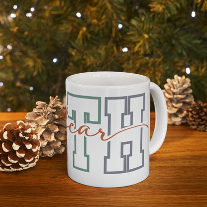 Mug with "Hoo" text in gray and teal, with pine cones and a blurred tree background.