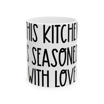 White mug with black text reading "IN THIS KITCHEN IS SEASONED WITH LOVE".