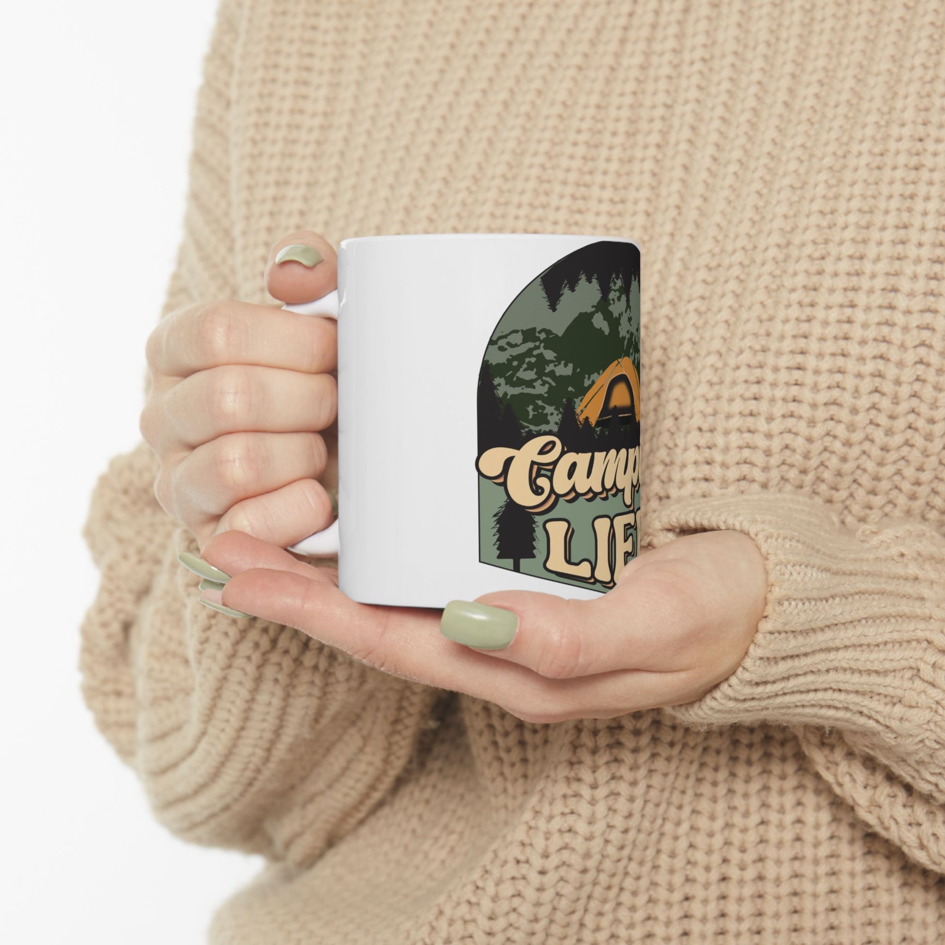 White mug with "Camp Life" text and forest silhouette, held by person.