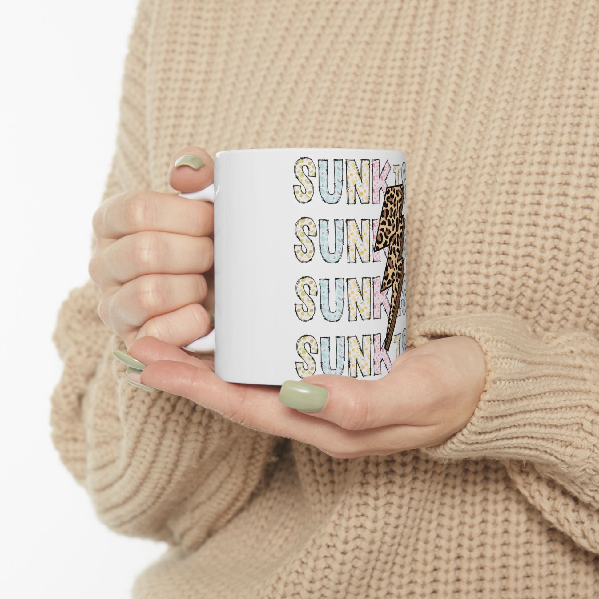 White mug with "SUNK" repeated in pastel colors and a giraffe pattern.