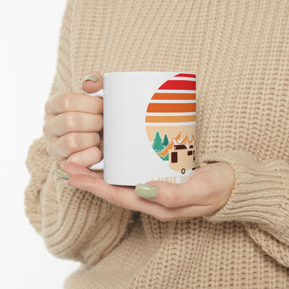 White mug with camper, trees, and mountain graphic with sunset.