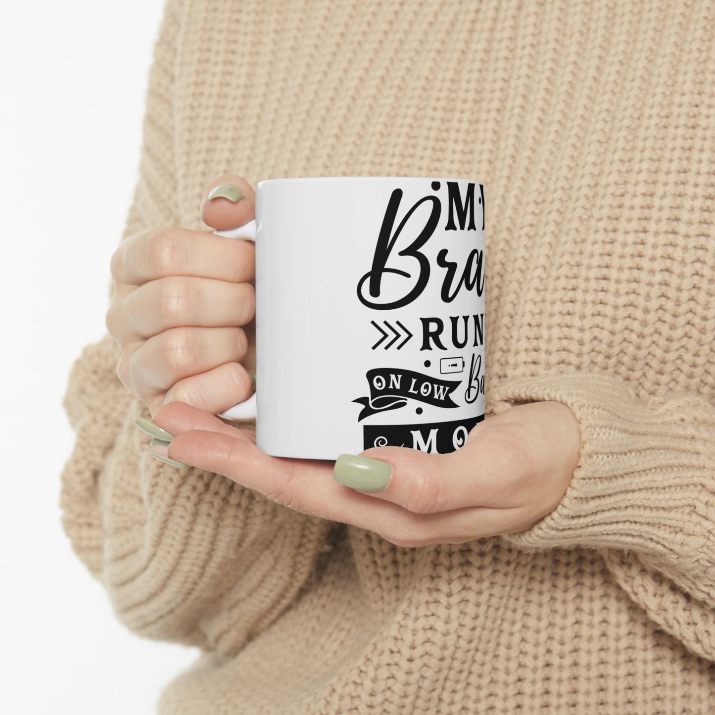 White mug with "My brain is running on low" text held by person.