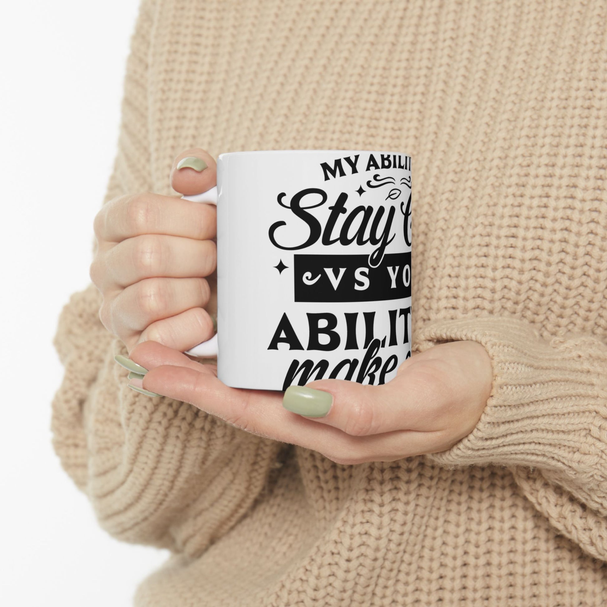 White mug with "My ability to stay vs. you ability to make" text held by hands.