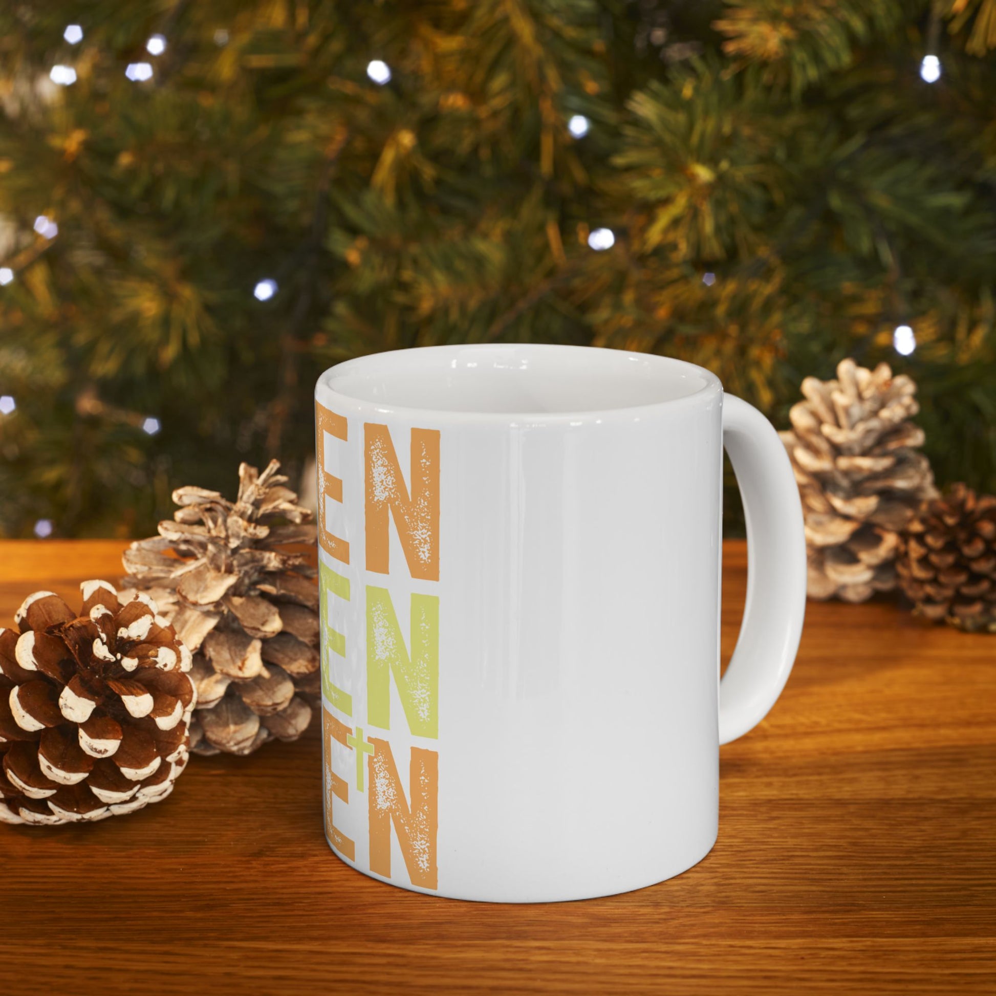 White mug with "Ren" in colorful letters against a blurred background of pinecones and fairy lights.