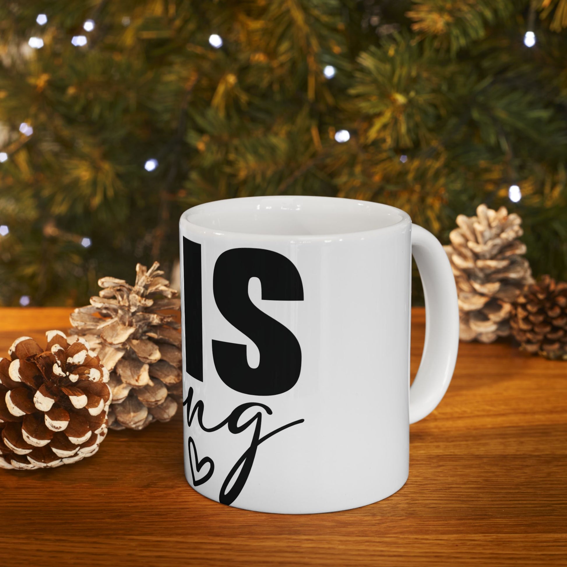 White mug with black text "This is" and a small heart, on a wooden table.