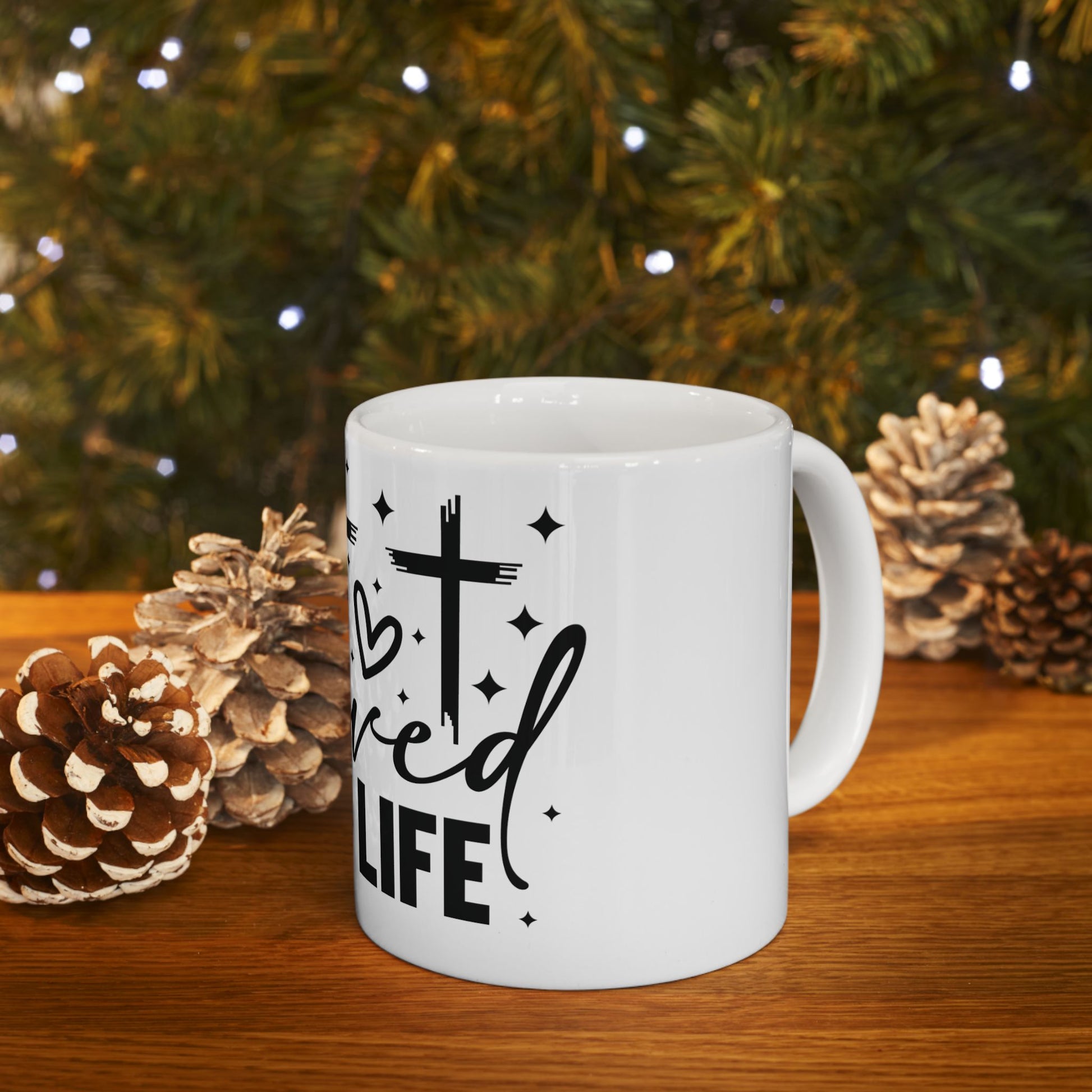White mug with "Blessed Life" and cross design on wooden surface.