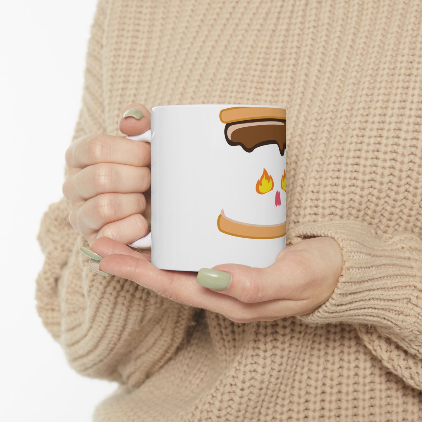 White mug with s'mores graphic, held by hands in a cream sweater.