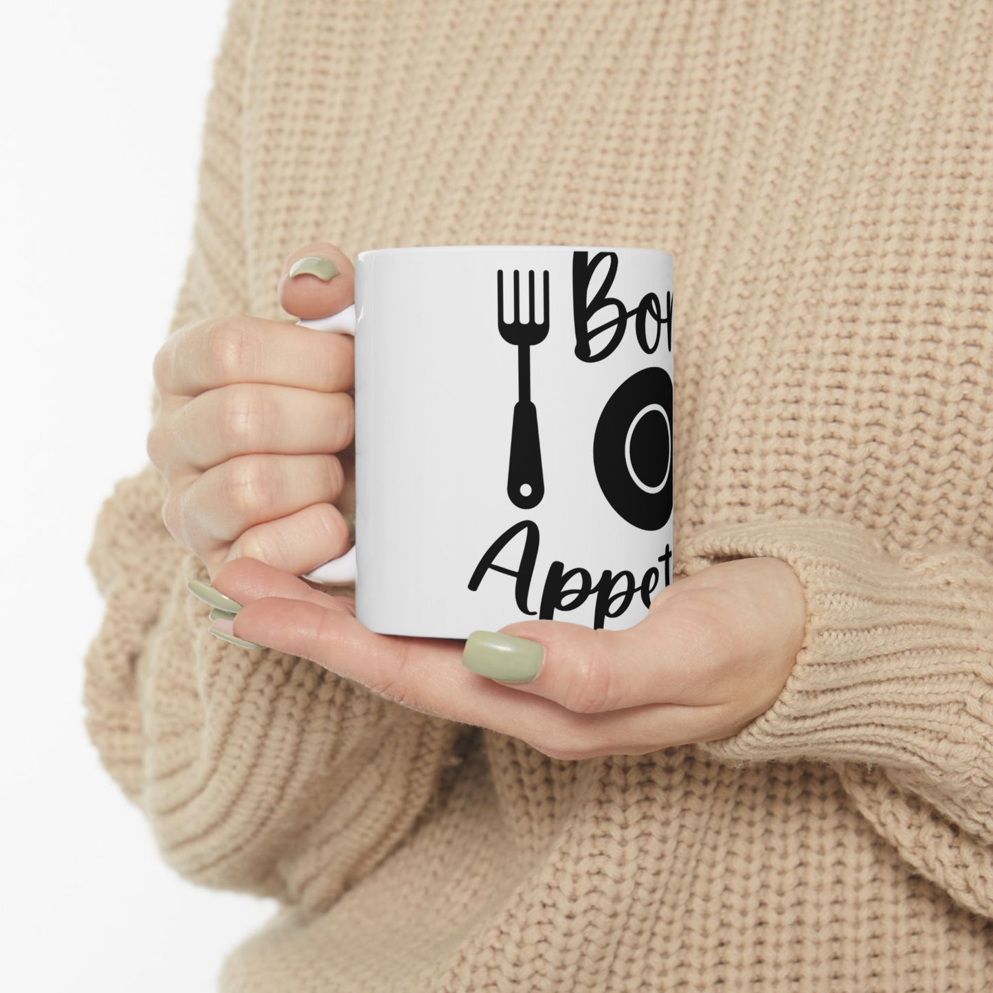 White mug with "Bon Appetit" text and silverware graphic, held by hands.
