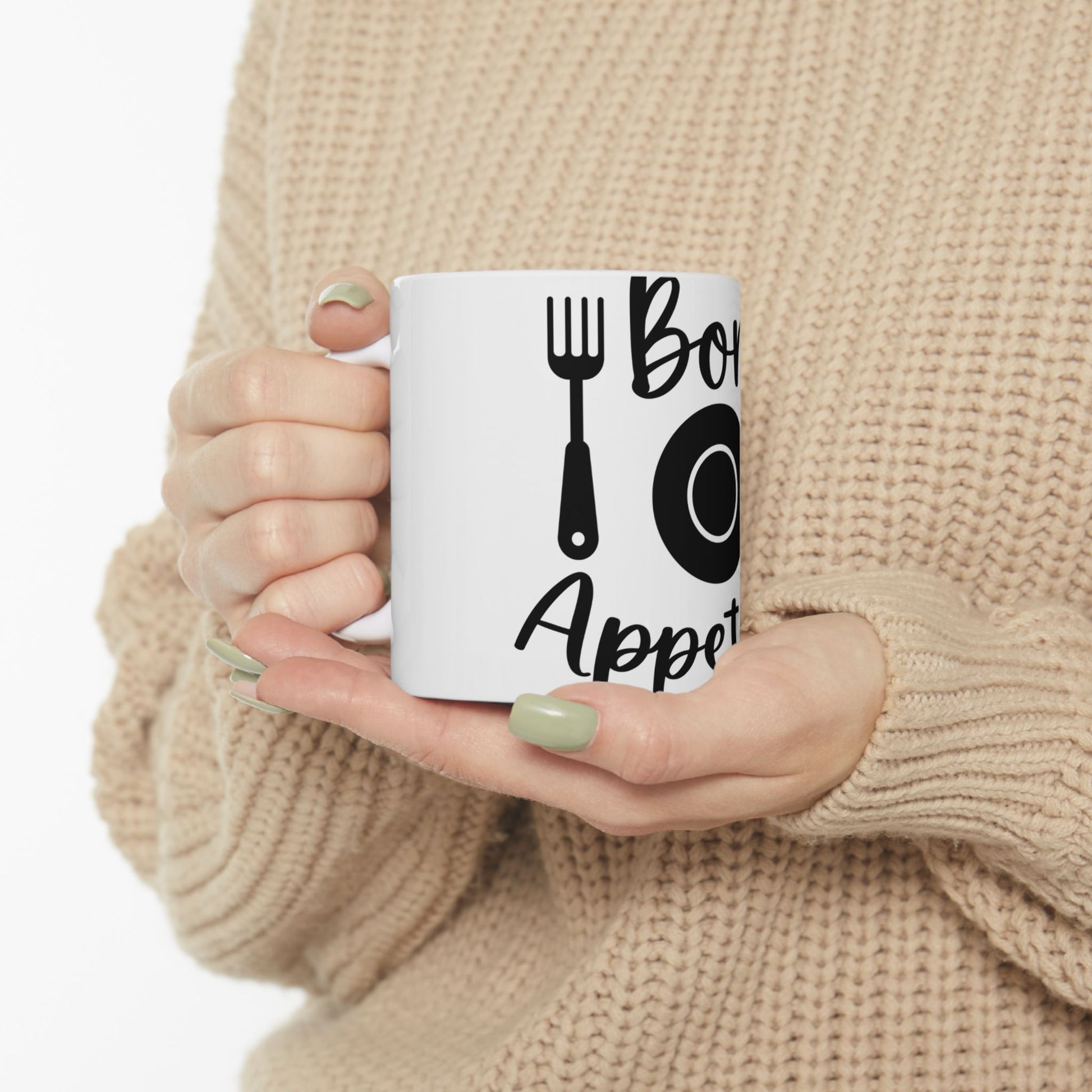 White mug with "Bon Appetit" text and silverware graphic, held by hands.
