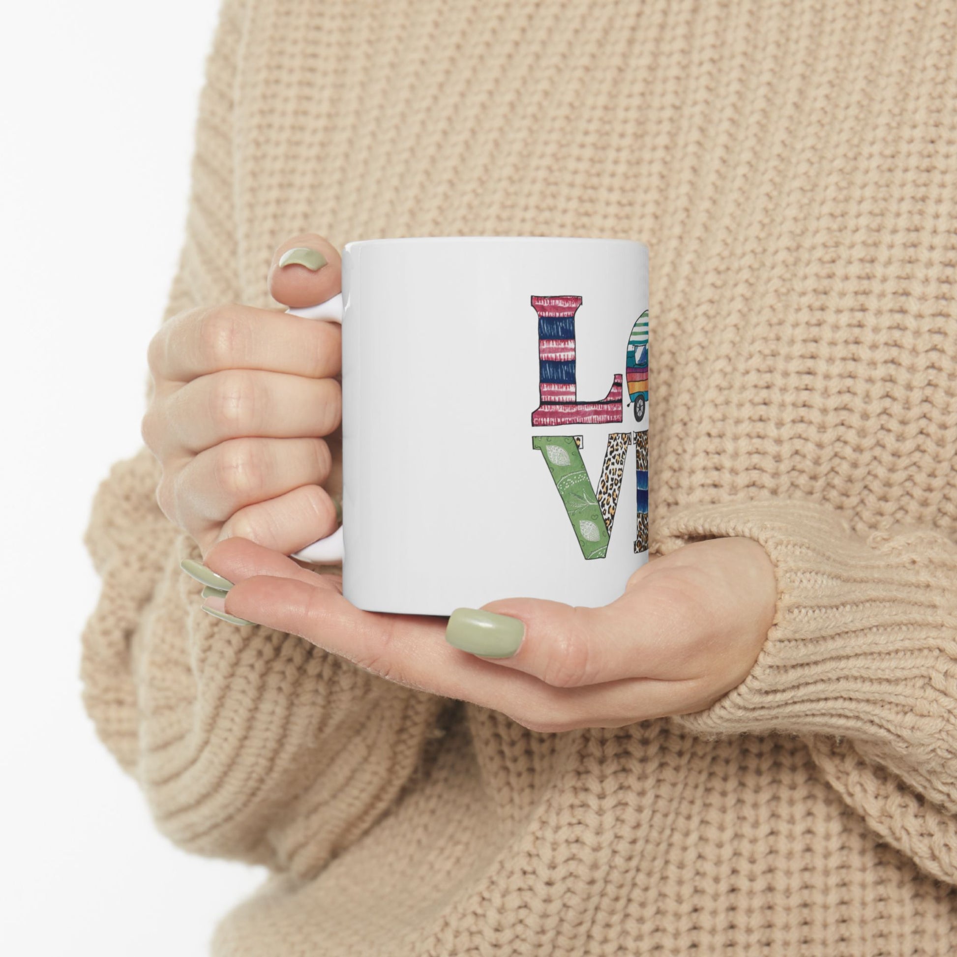 White mug with "LOVE" in a collage of patterned letters held by hands.