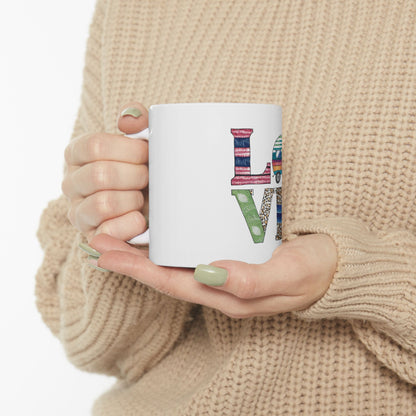 White mug with "LOVE" in a collage of patterned letters held by hands.
