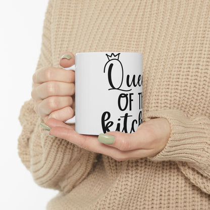 White mug with "Queen of the kitchen" text held by hands wearing a beige sweater.