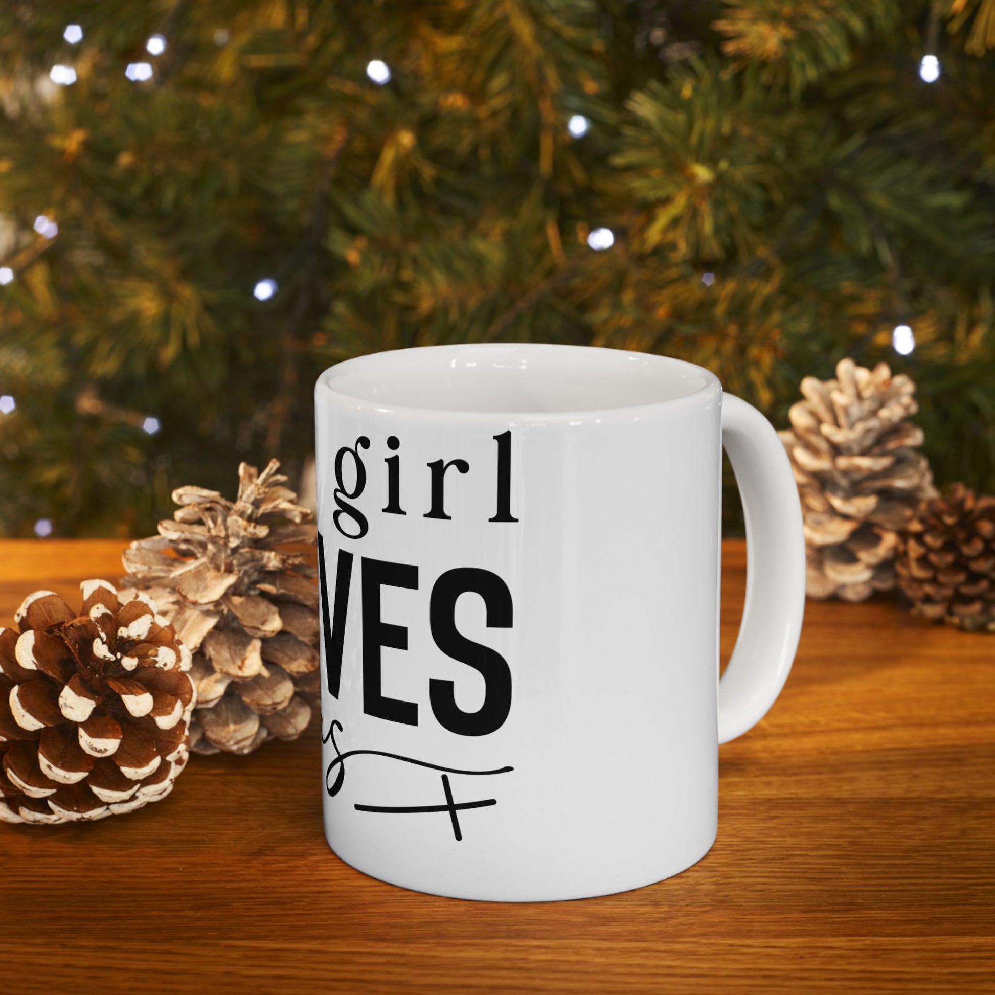 White mug with "girl" and "VES" text, surrounded by pinecones and greenery.