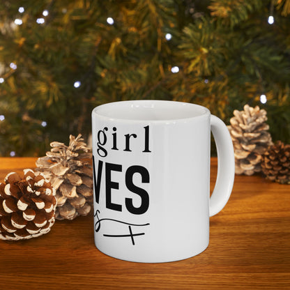 White mug with "girl" and "VES" text, surrounded by pinecones and greenery.