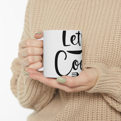 White mug with "Let's Cook" in black text, held by a person.