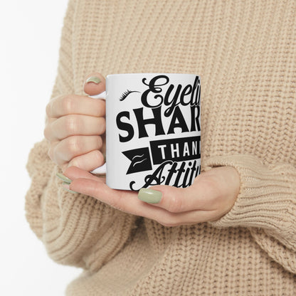 White mug held by person with text "Eyeliner Sharper Than Attitude".