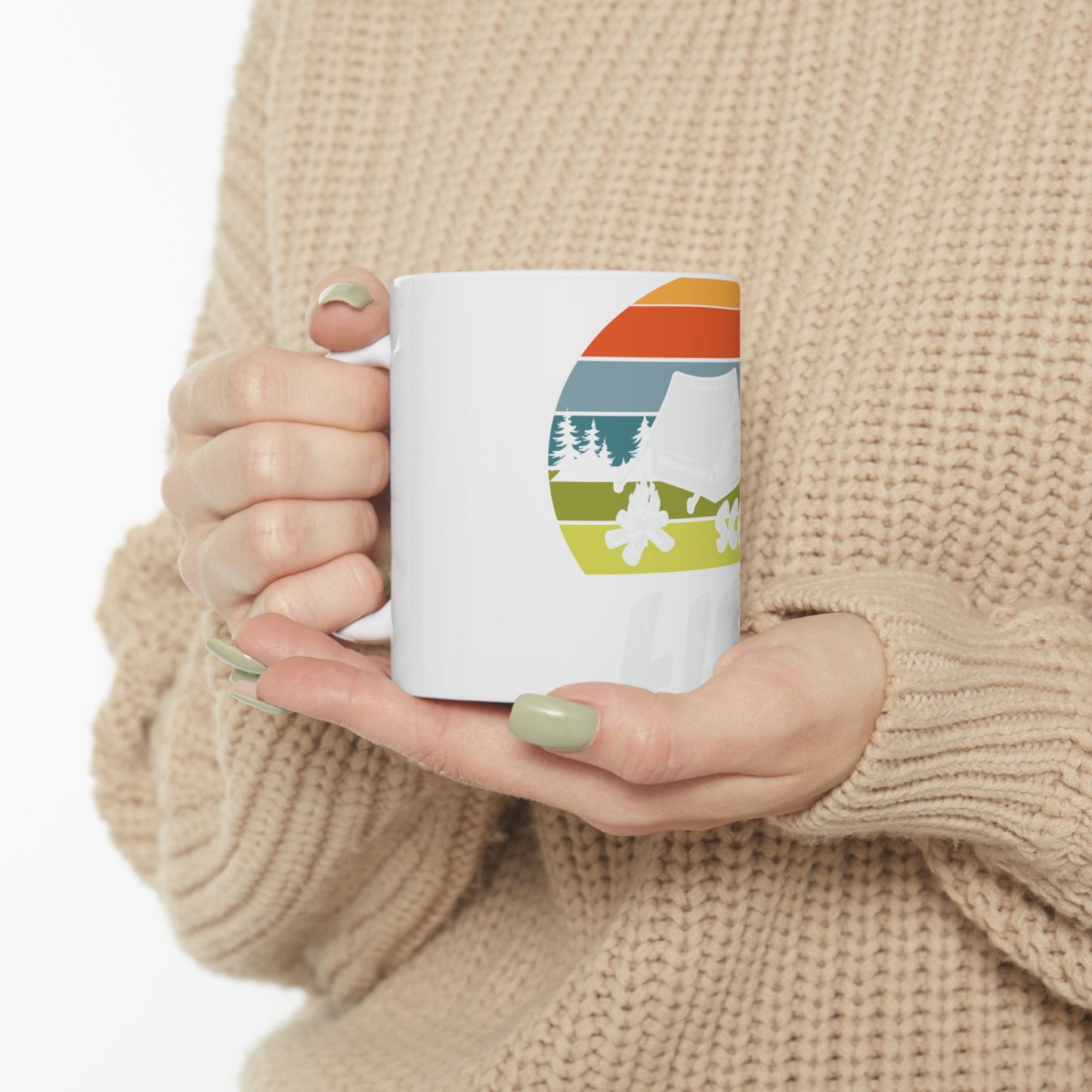 White mug with retro camping graphic on a beige sweater background.