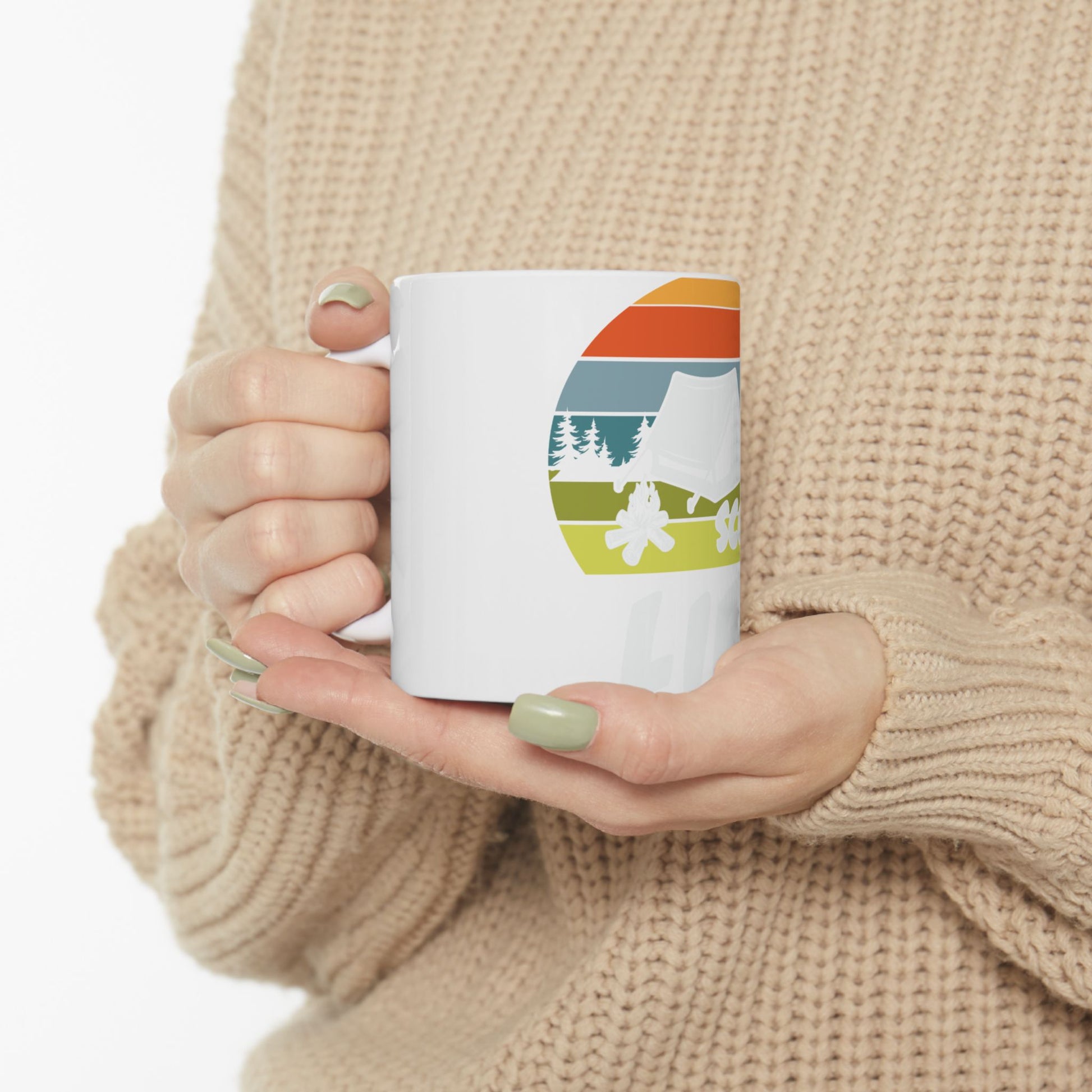 White mug with retro camping graphic on a beige sweater background.