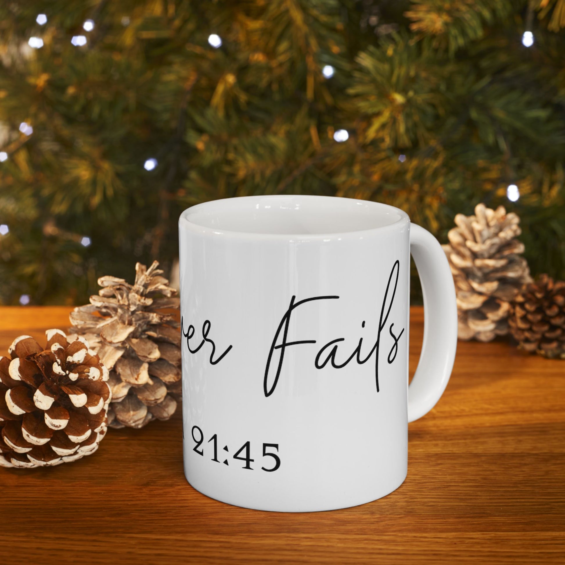 White mug with "Never Fails 21:45" text, on a wooden surface with pinecones and lights.