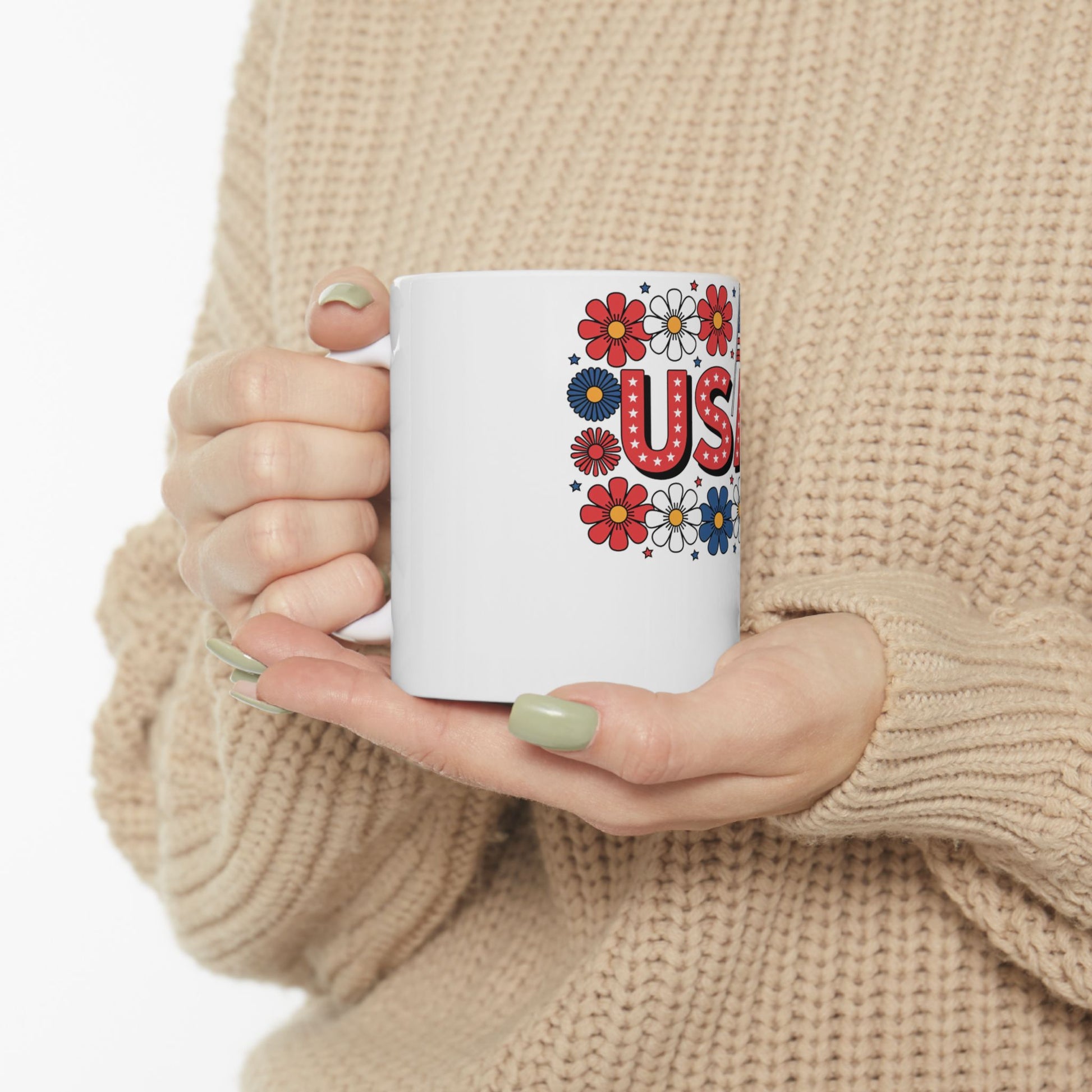 White mug with "USA" in colorful floral lettering held by hands.