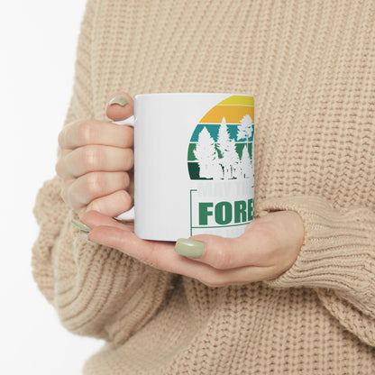 White mug with green forest sunset graphic and text.