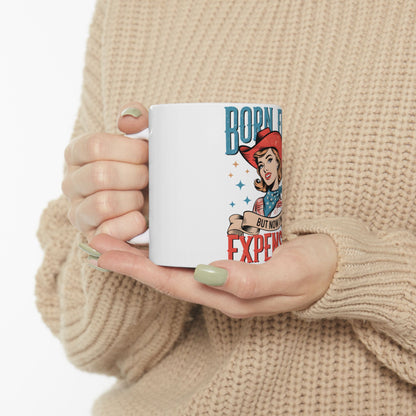 White mug with "Born Free But Now Expensive" text and retro woman graphic.