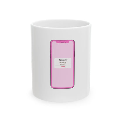 White mug with pink phone graphic showing "Reminder: Be kind to yourself".